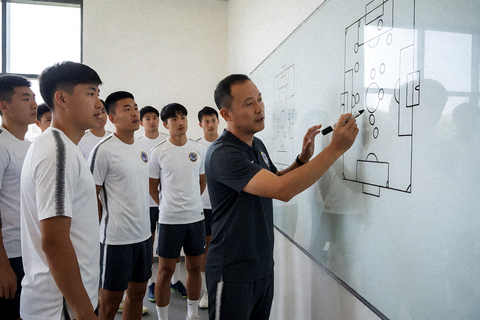 足球教练战术板分析场景，教练在白板上绘制战术跑位线路指导球员